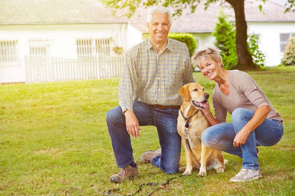 Happy,Senior,Couple,Sitting,With,House,And,Labrador,Retriever,In