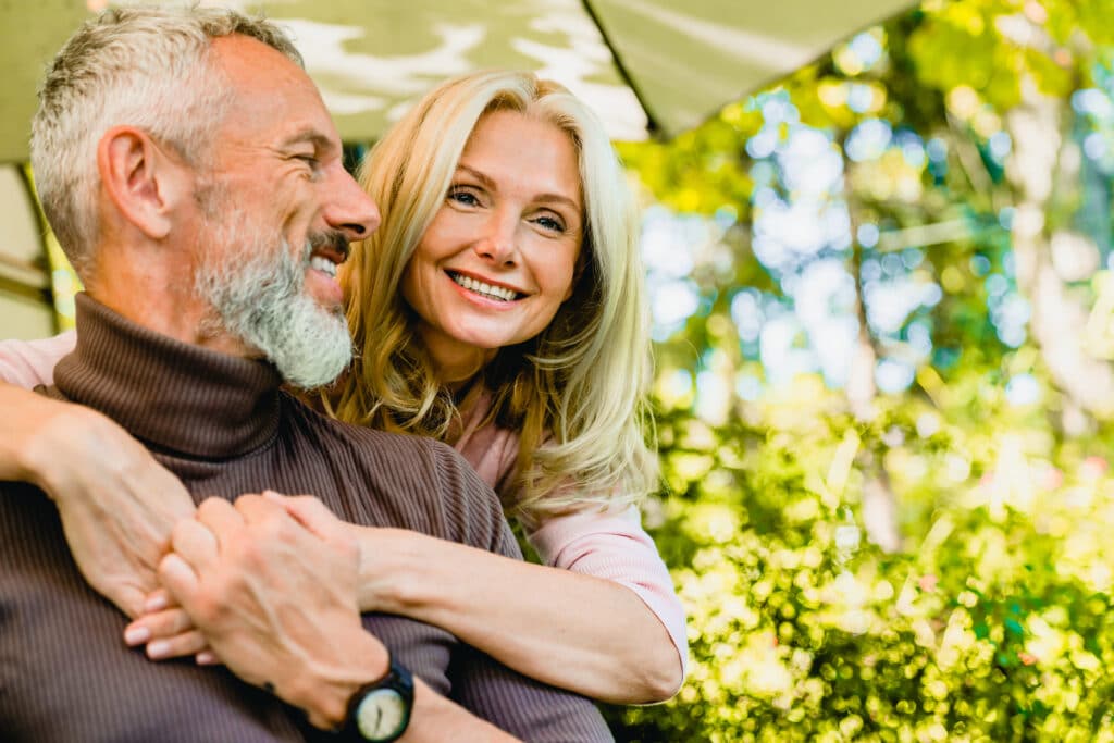 Beautiful,Aged,Blond,Woman,Hugging,Her,Grey-haired,Husband,In,Park
