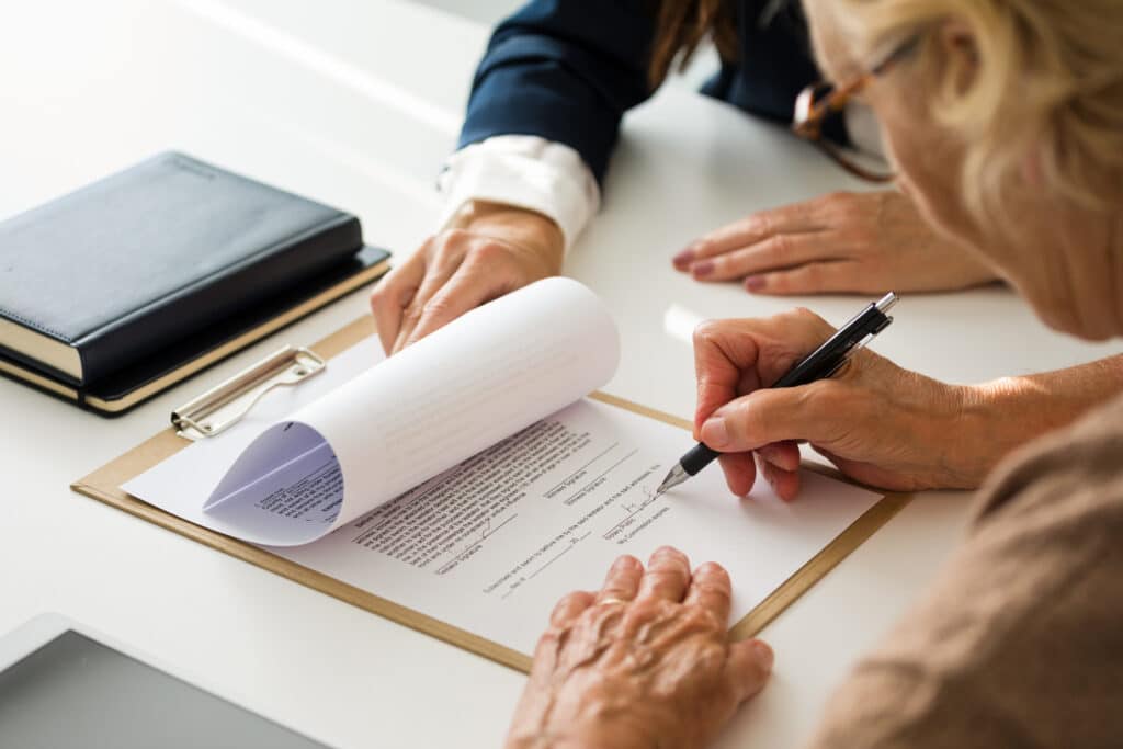 Senior woman signing estate planning documents with an elder law attorney.